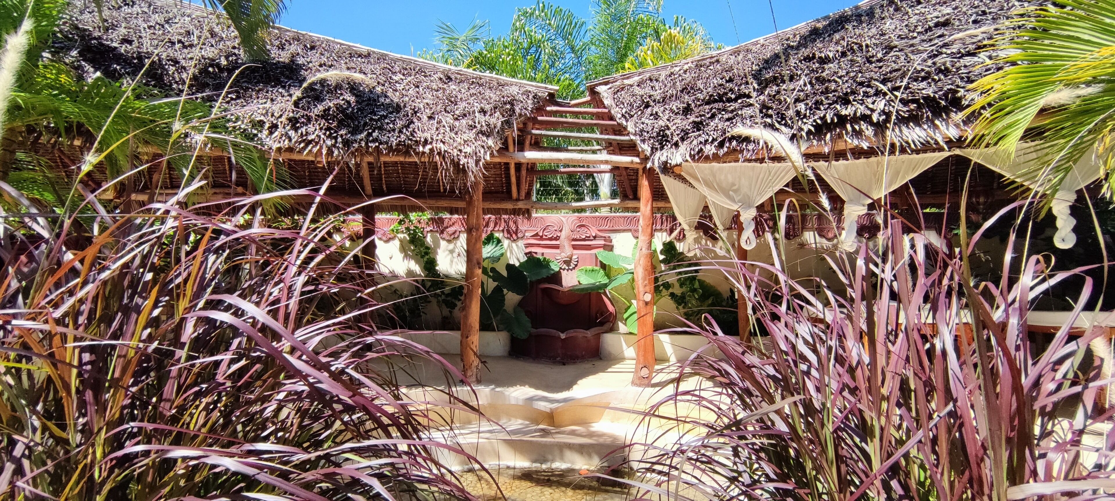 A tropical garden with a wooden pergola and thatched roof structures.