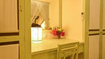 Una habitación con un escritorio de madera, un espejo y una mesita de noche con una lámpara y flores.