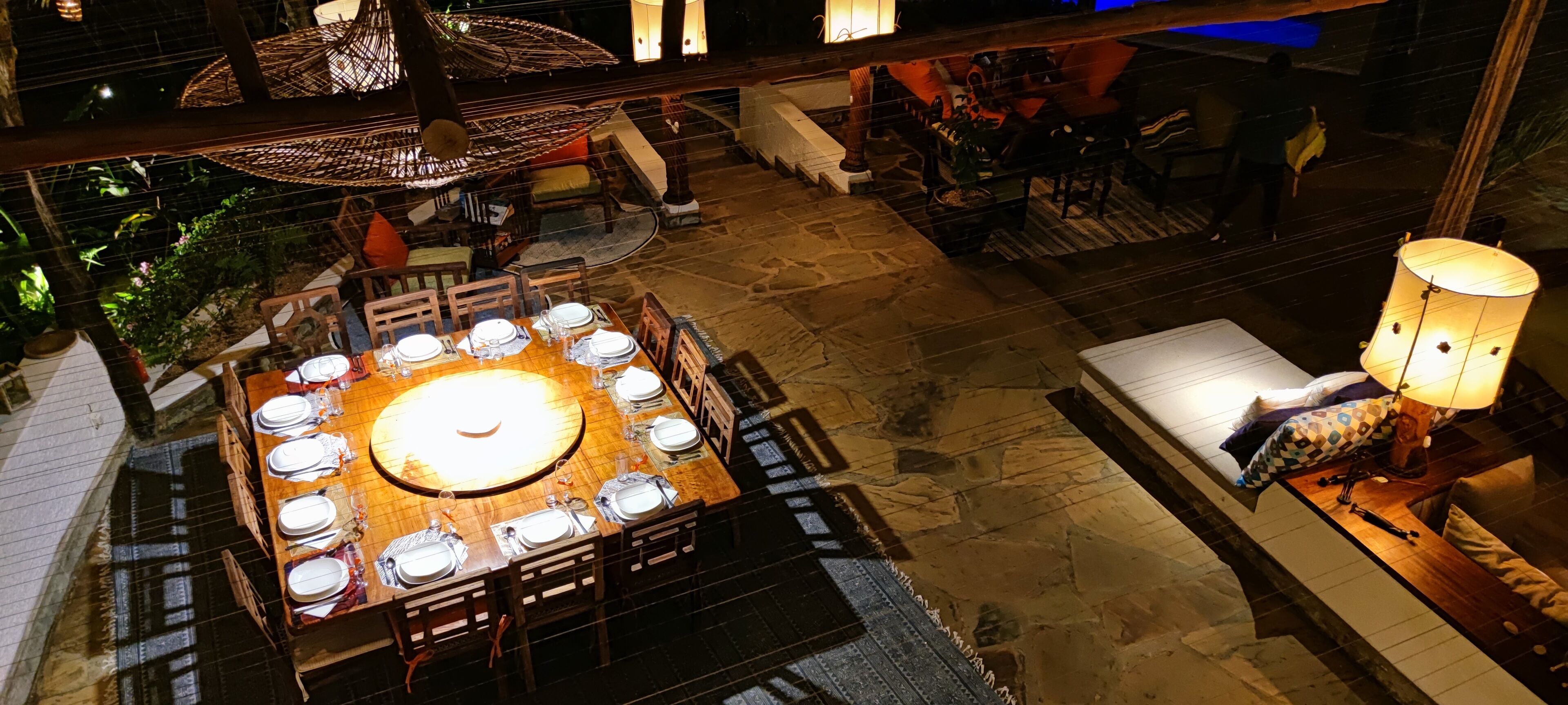 An outdoor dining area with a round table set for a meal, surrounded by wooden chairs.