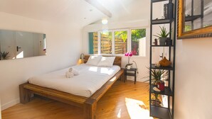 Une chambre avec un lit en bois, une table de chevet, une étagère avec des plantes et une fenêtre donnant sur un paysage verdoyant.