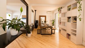 Un espace de salle à manger moderne avec une table en bois dressée pour quatre personnes, entourée d’étagères blanches où sont disposés des livres et des plantes.