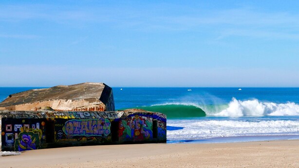 Une plage où les rochers sont couverts de graffitis et où les vagues déferlent sur le rivage.