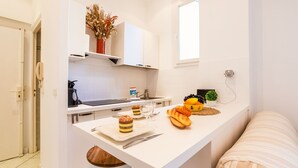 A compact kitchen with white cabinets, a small island with food items, a coffee machine, and a window providing natural light. - LE FLORIDA AP4340 By Riviera Holiday Homes (Villefranche-sur-Mer)