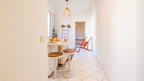 A narrow hallway with a white tiled floor, a small table with stools, a hanging light fixture, and a red chair. - LE FLORIDA AP4340 By Riviera Holiday Homes (Villefranche-sur-Mer)