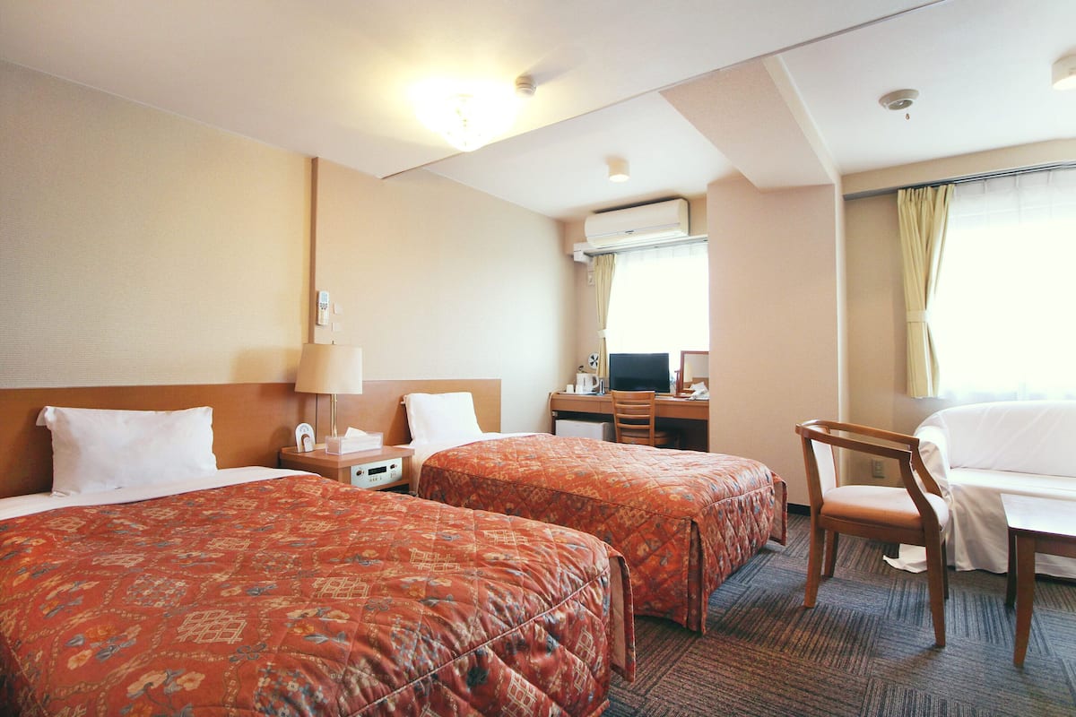 Hotellihuone, jossa on kaksi sänkyä, työpöytä, tuoli ja ilmastointilaite.