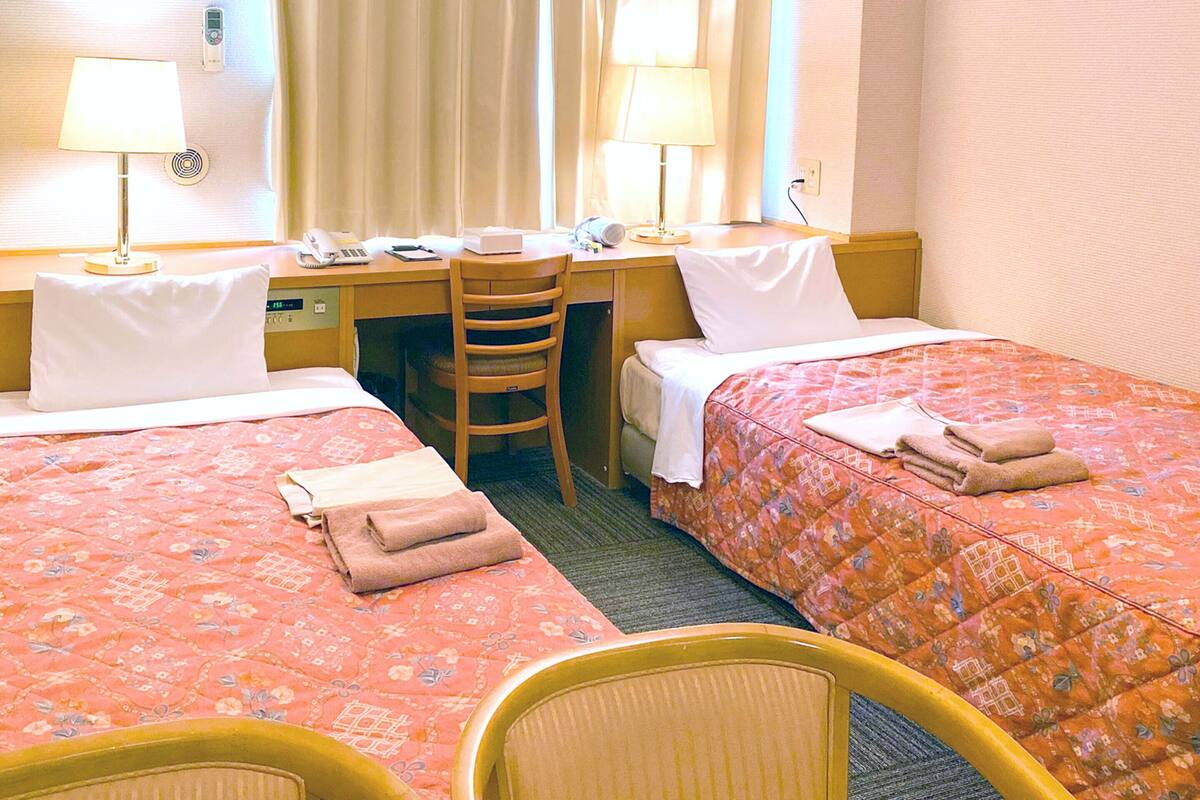 Hotellihuone, jossa on kaksi sänkyä, työpöytä, tuoli ja puhelin.