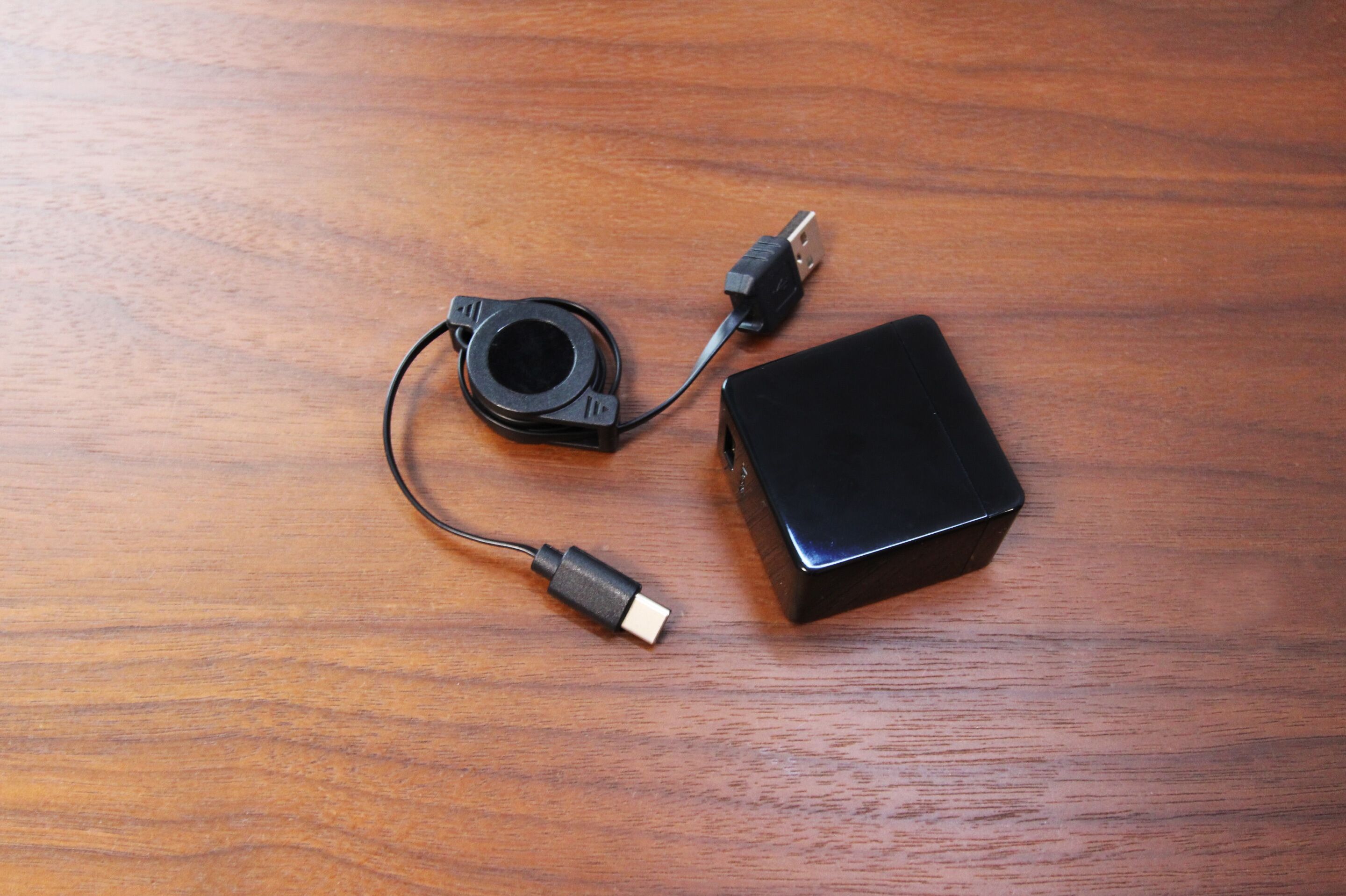 A black electronic device with two cables on a wooden surface.