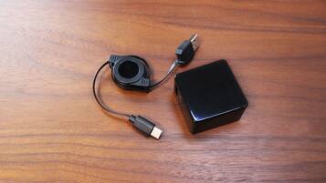 A black electronic device with two cables on a wooden surface.