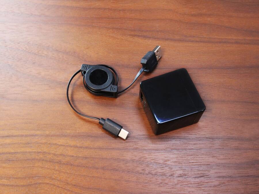 A black electronic device with two cables on a wooden surface.
