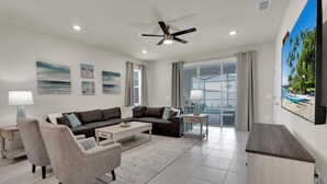 A modern living room with a sectional sofa, a coffee table, a TV, and a balcony with a view. - Luxury Private House With Pool on Windsor Island, Orlando House 6155 (Davenport)