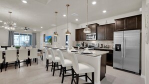 A modern kitchen with dark wood cabinets, stainless steel appliances, and a central island with white bar stools. - Luxury Private House With Pool on Windsor Island, Orlando House 6155 (Davenport)