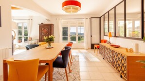 A dining area with a wooden table, yellow chairs, a red pendant light, and a view through glass doors to an outdoor area. - Comfortable villa 10 minutes from the beach (La Garde)
