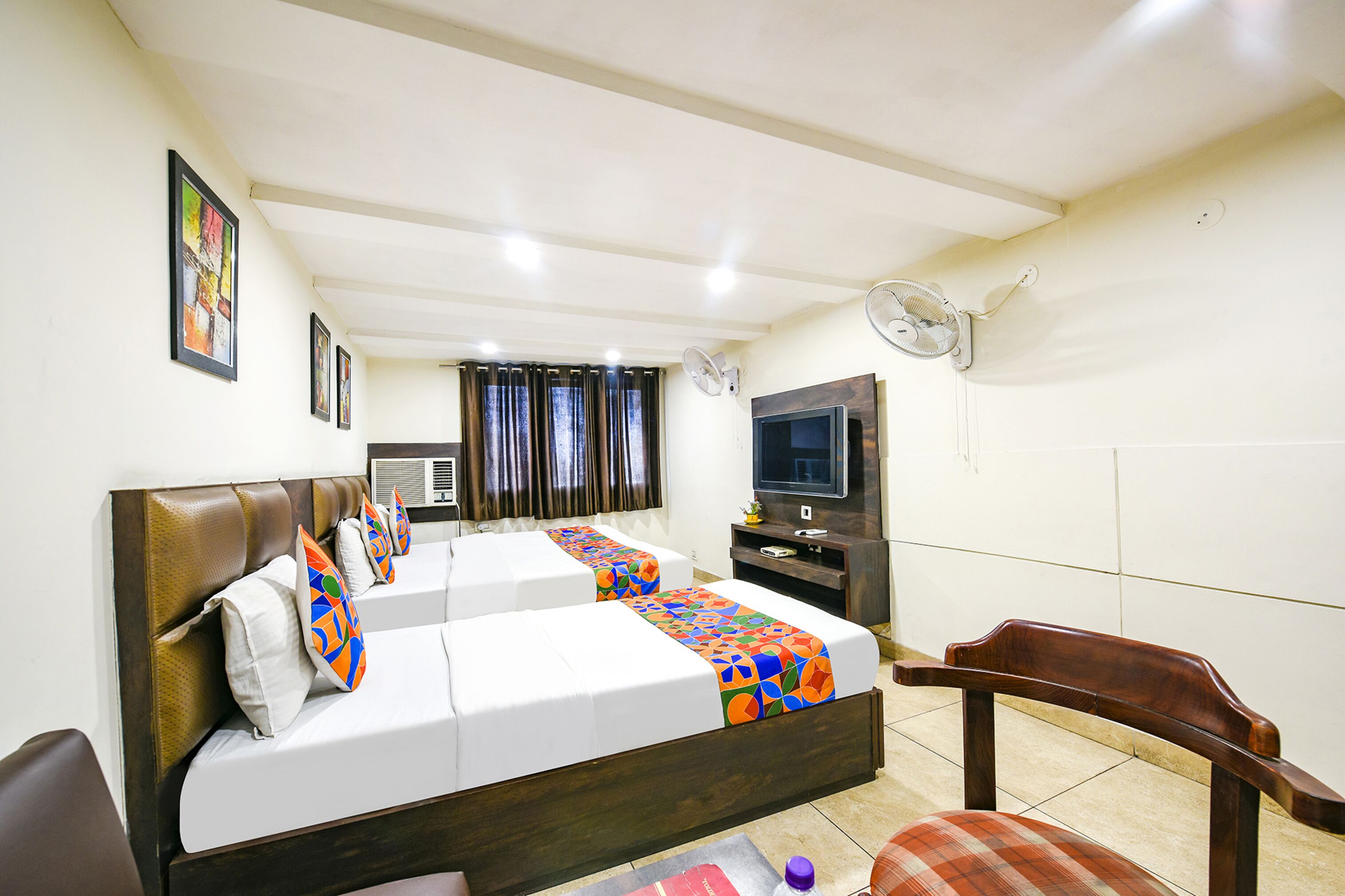 A hotel room with two beds, a TV, a fan, and a chair.