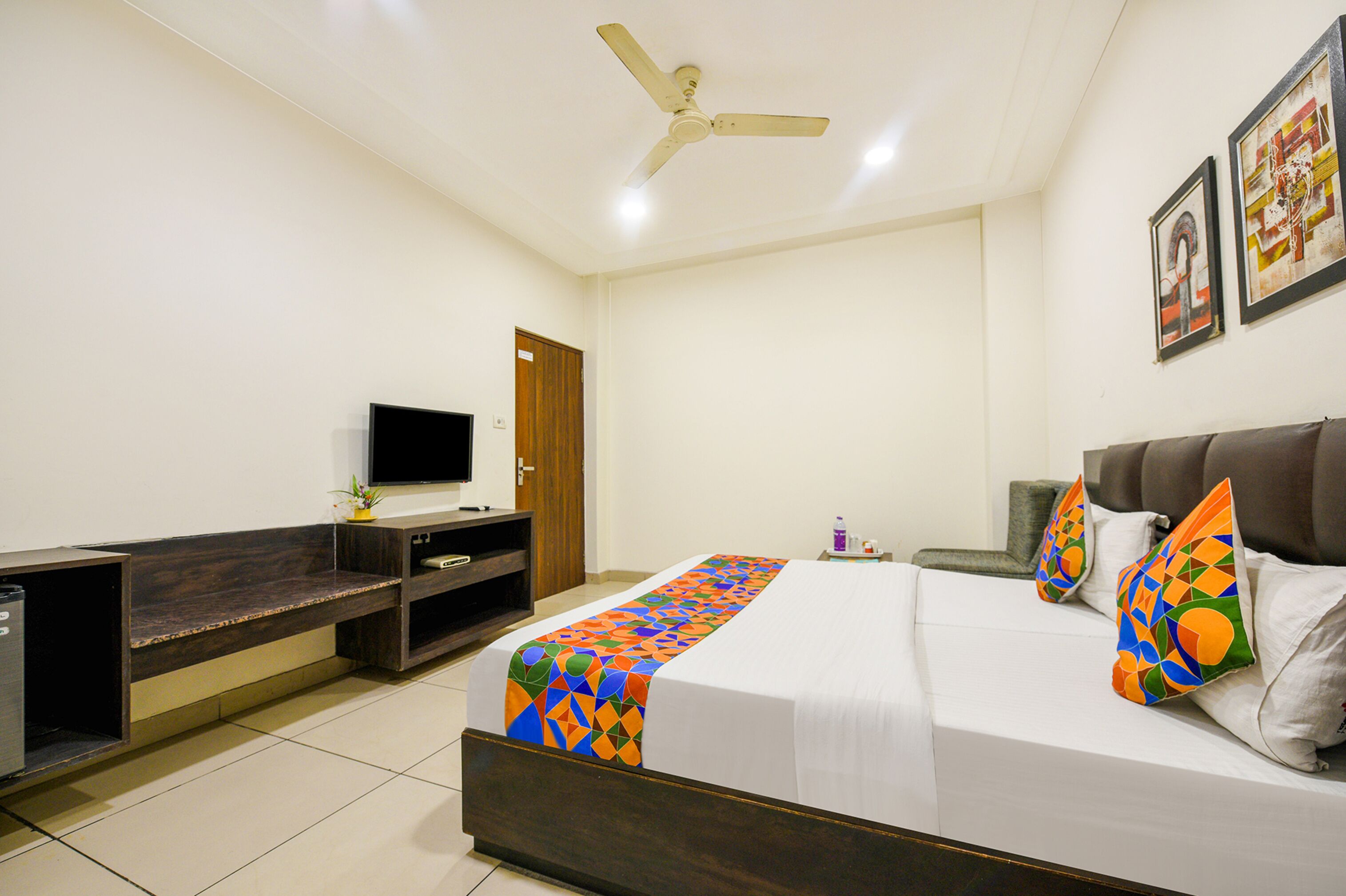 Quarto de hotel com uma cama, televisão, escrivaninha e ventoinha no teto.
