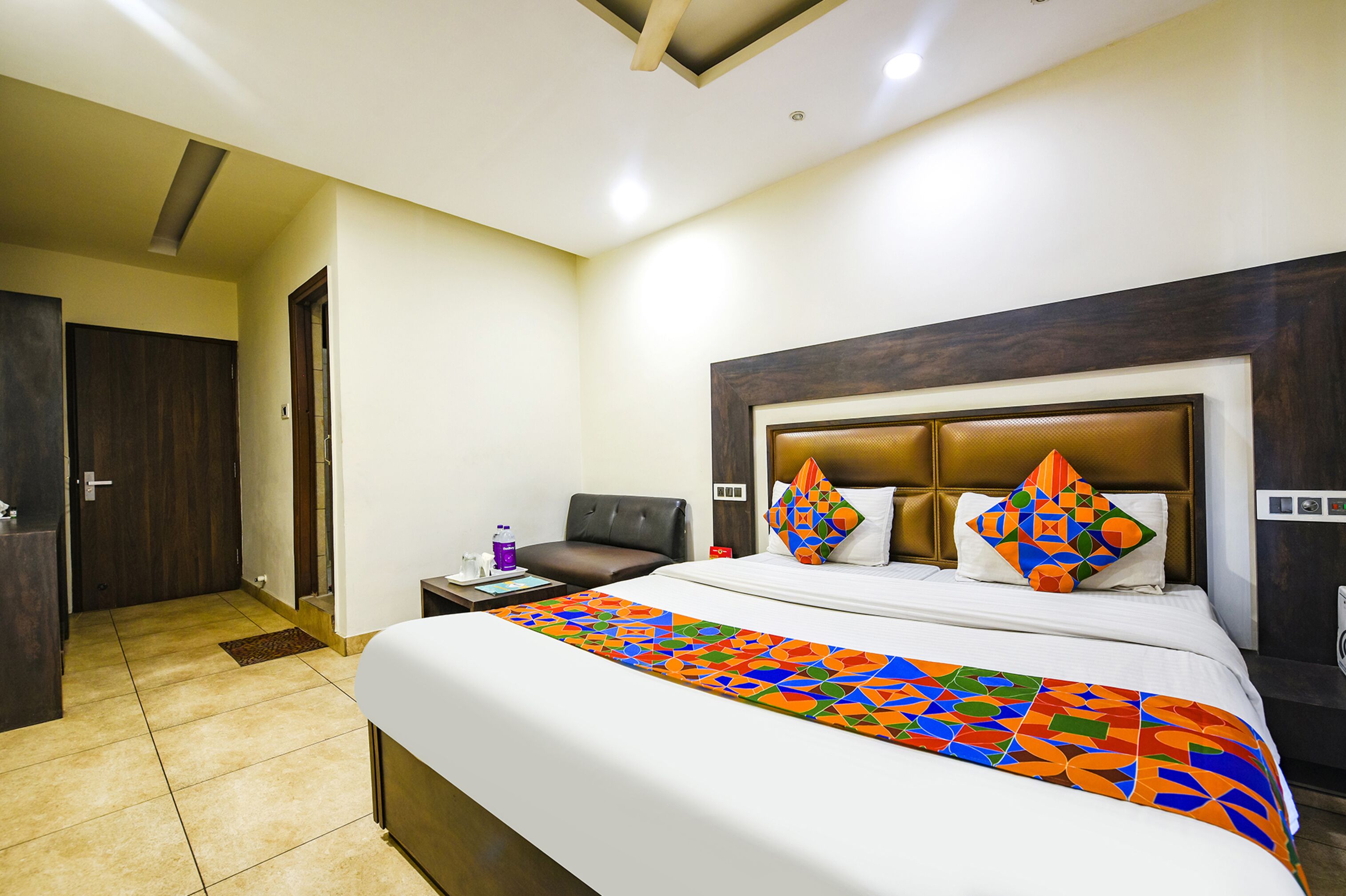 A hotel room with a large bed, a headboard, a nightstand, and a door.