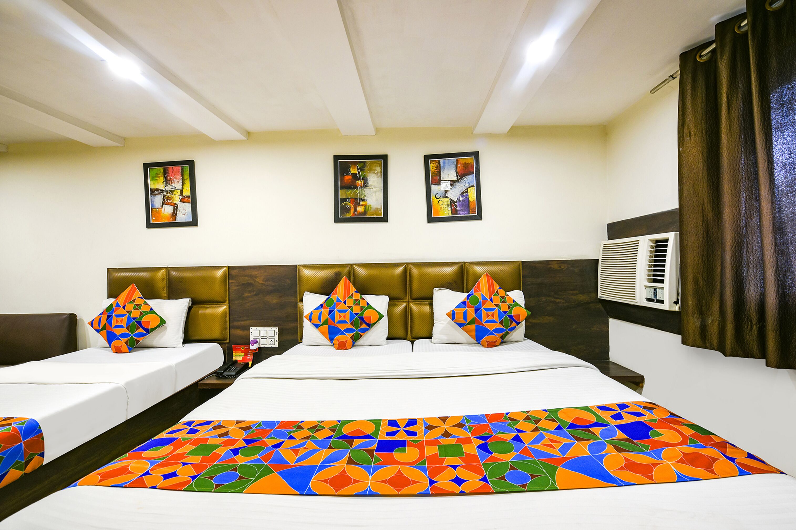 Een hotelkamer met een groot bed, twee kleinere bedden, een hoofdbord, een airconditioning en kunst aan de muur.