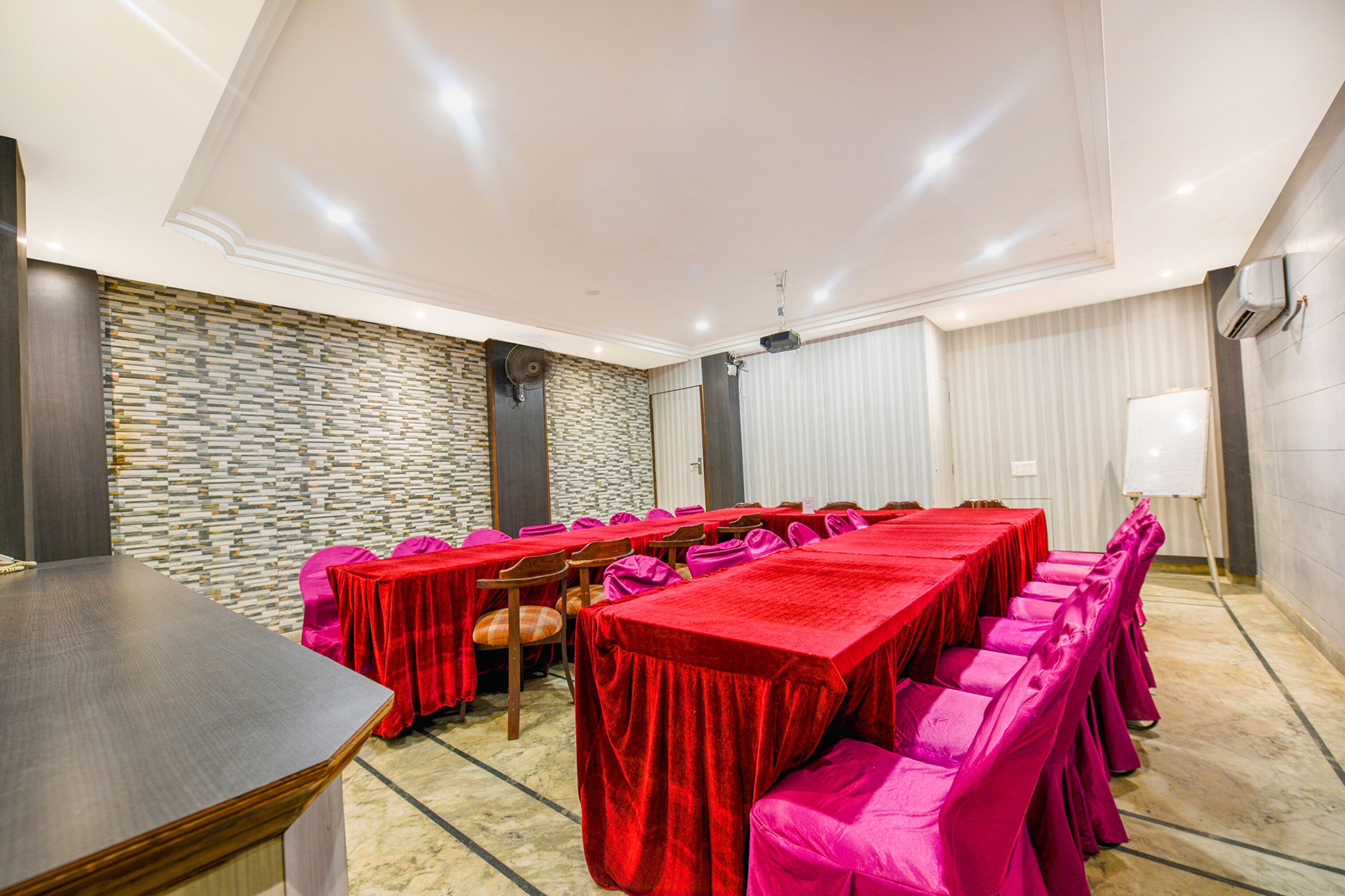 A conference room with a long table, red tablecloths, and pink chairs.