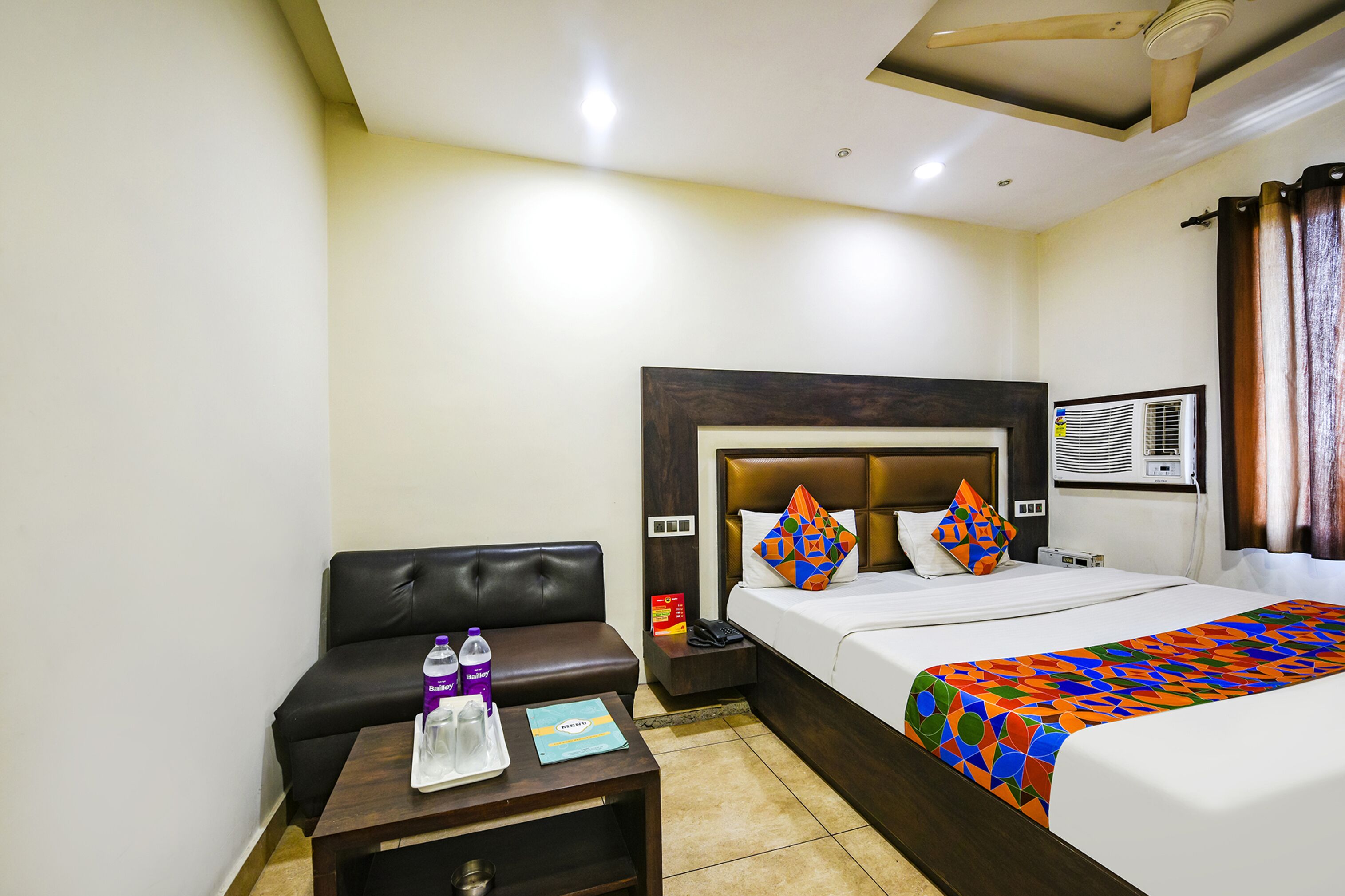 A hotel room with a bed, a sofa, a nightstand, a table, and a ceiling fan.