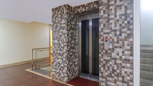 An elevator with a checkered tile wall, a red doormat, and a metal handrail.