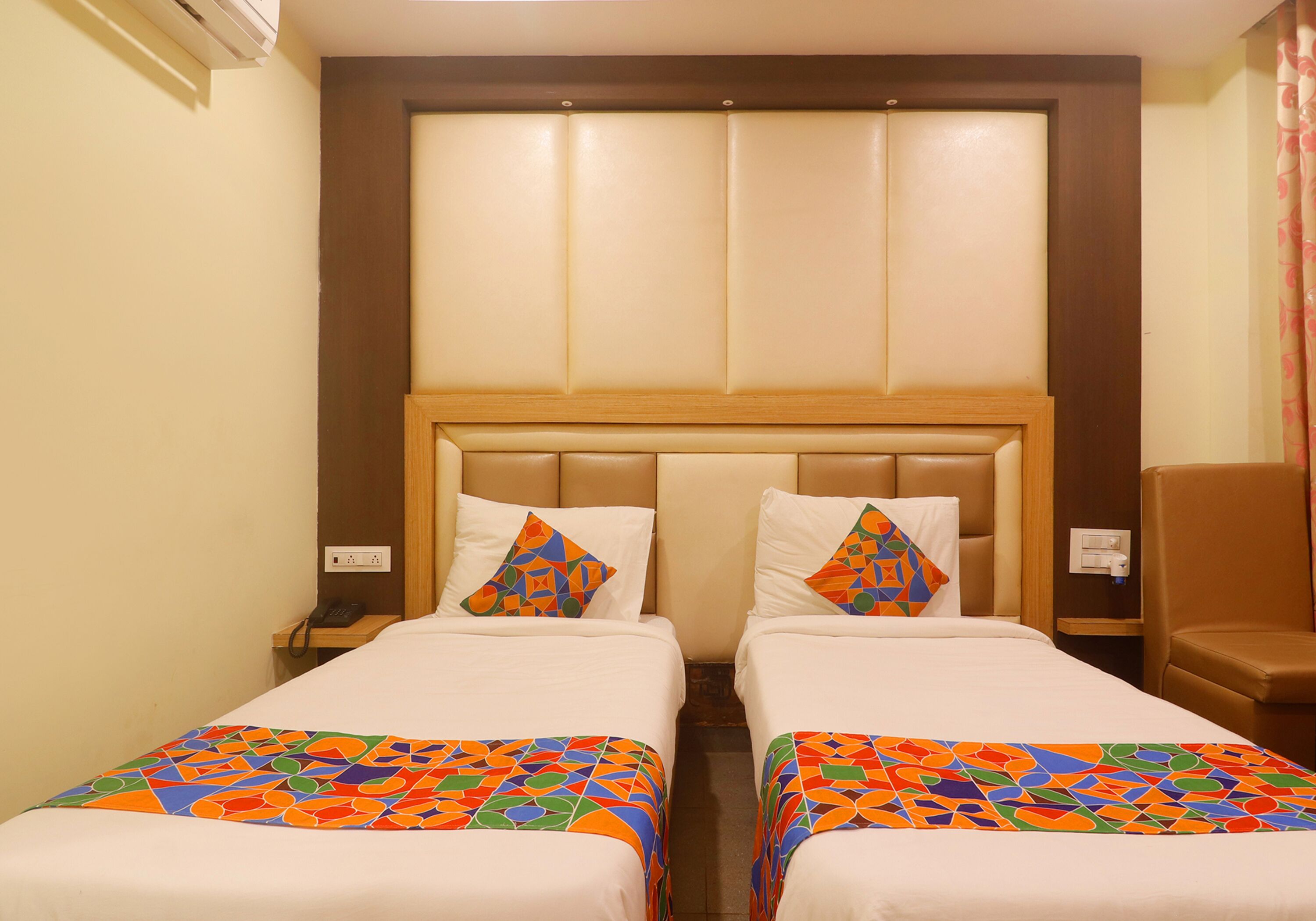 A hotel room with two single beds, a wooden headboard, and a small wooden nightstand with a phone.