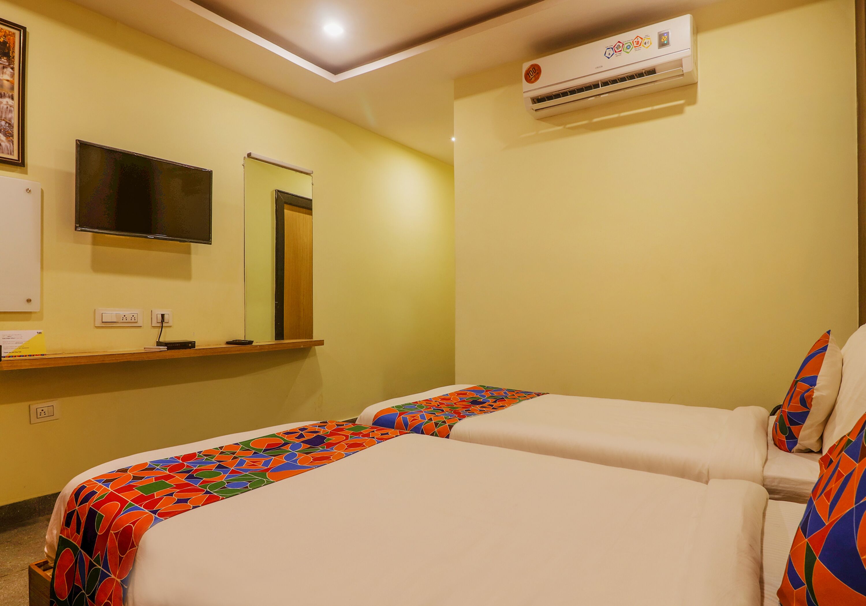 A hotel room with two beds, a TV, an air conditioner, and a mirror.