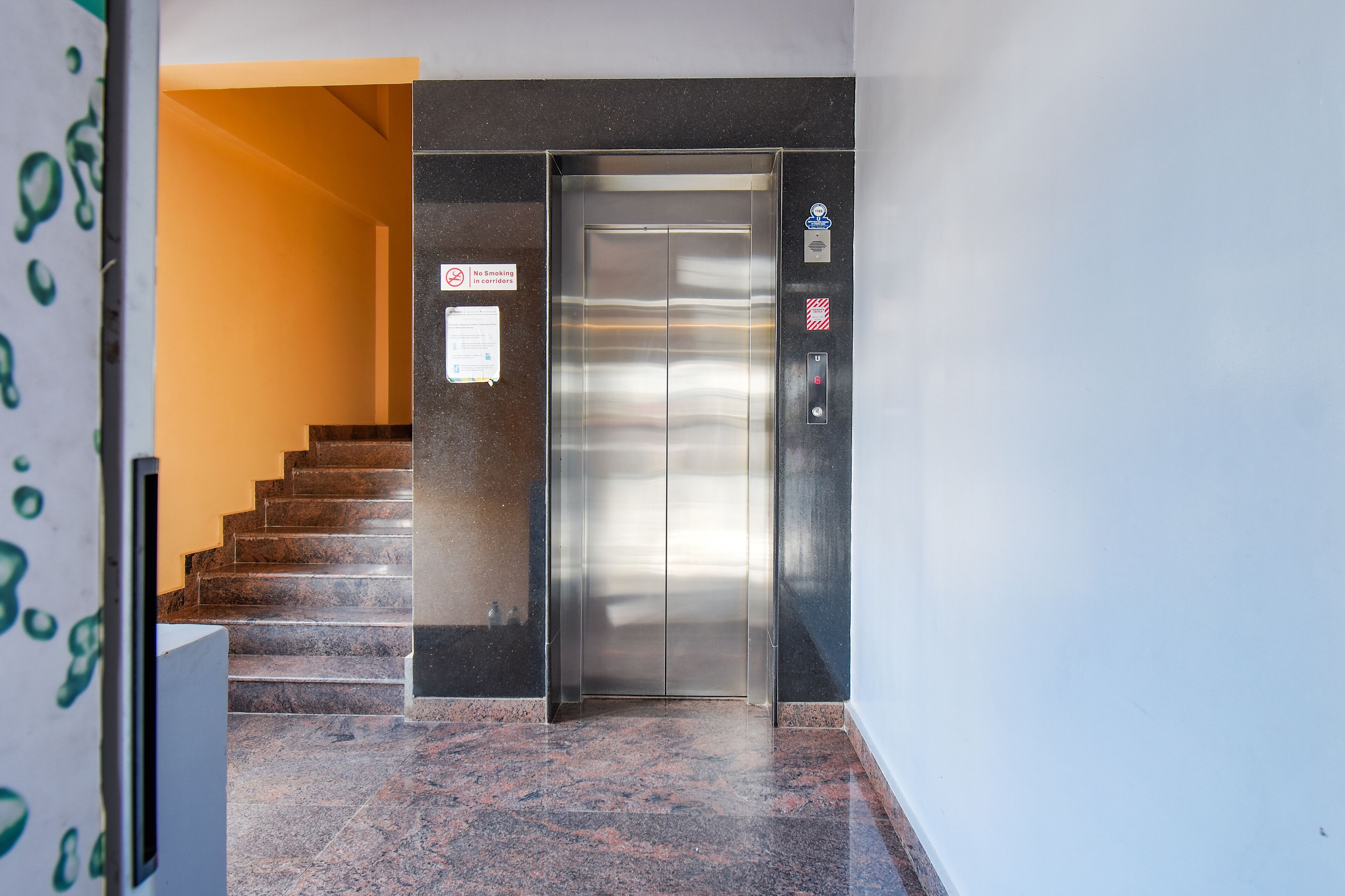 An elevator with a stainless steel finish, a no-smoking sign, and a fire alarm button.