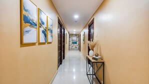 A hallway with a tiled floor, framed artwork on the walls, and a console table with decorative items. - Fabhotel Rotano Suites (Bengaluru)