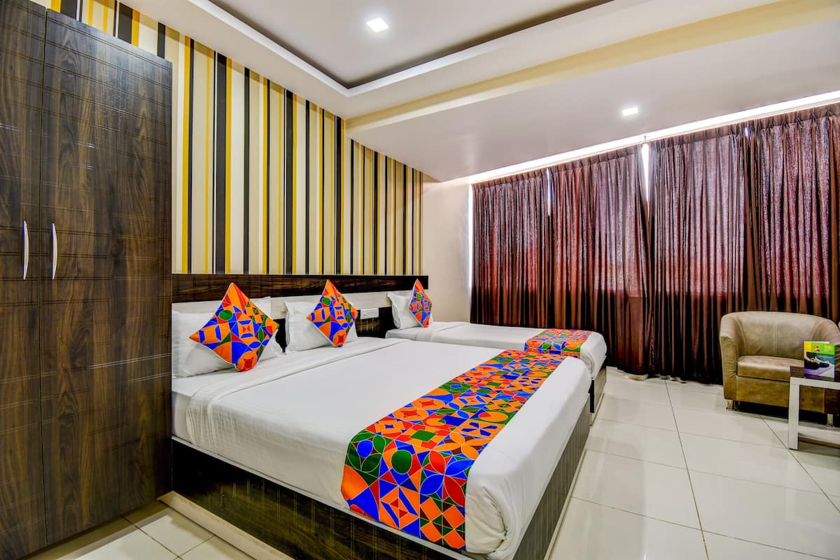 Habitación de hotel con dos camas, un armario, una silla y un ventanal con cortinas.