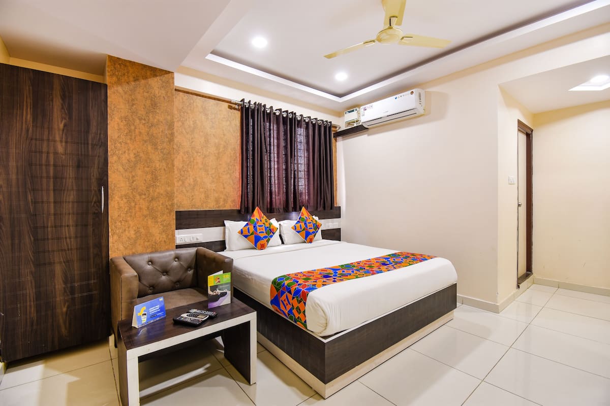 Habitación de hotel con cama, escritorio, silla, armario y ventilador de techo.