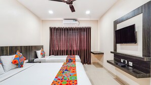 A hotel room with two beds, a ceiling fan, an air conditioning unit, a TV mounted on the wall, and a decorative pillow on one bed. - Fabhotel Rove Inn & Suites (Bengaluru)