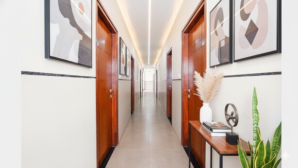 A hallway with wooden doors, framed artwork, a vase with pampas grass, and a small table with books and a decorative object. - Fabhotel Rove Inn & Suites (Bengaluru)