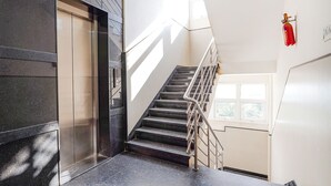 A modern staircase with a metal railing, a fire extinguisher mounted on the wall, and a door leading to an elevator. - Fabhotel Rove Inn & Suites (Bengaluru)