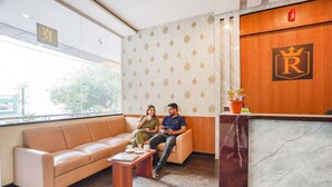 A reception area with a sofa, a coffee table, and a reception desk with a logo. - Fabhotel Rove Inn & Suites (Bengaluru)