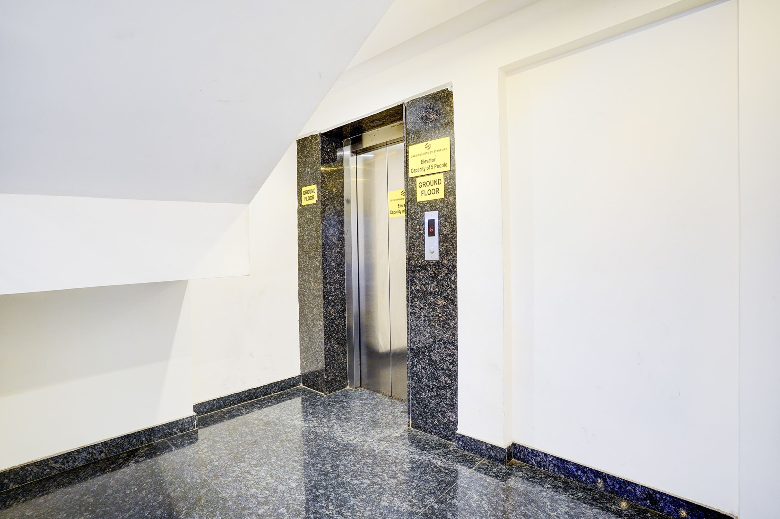 An elevator in a hallway with granite walls and a marble floor.