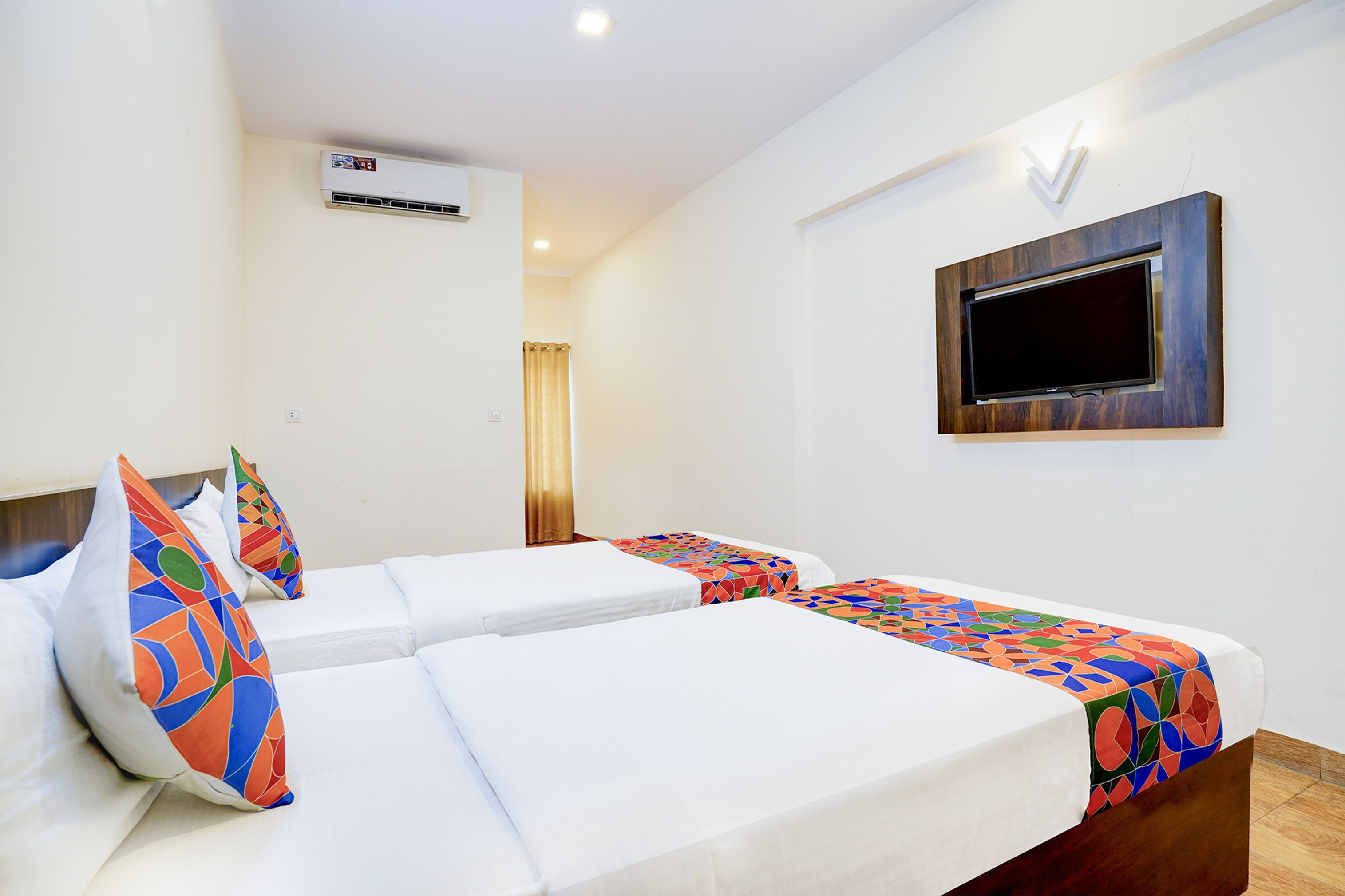 A hotel room with two beds, a TV mounted on the wall, and an air conditioning unit.