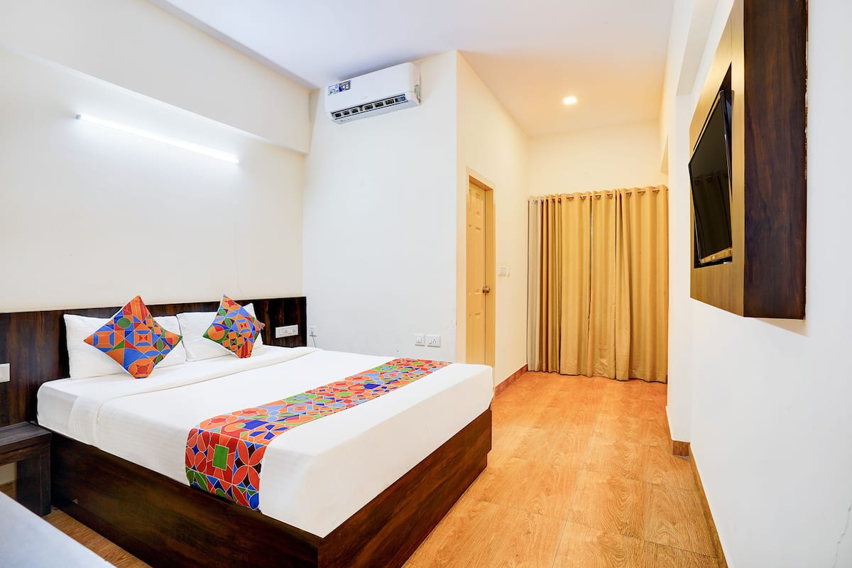 A hotel room with a bed, a TV mounted on the wall, and a wooden floor.
