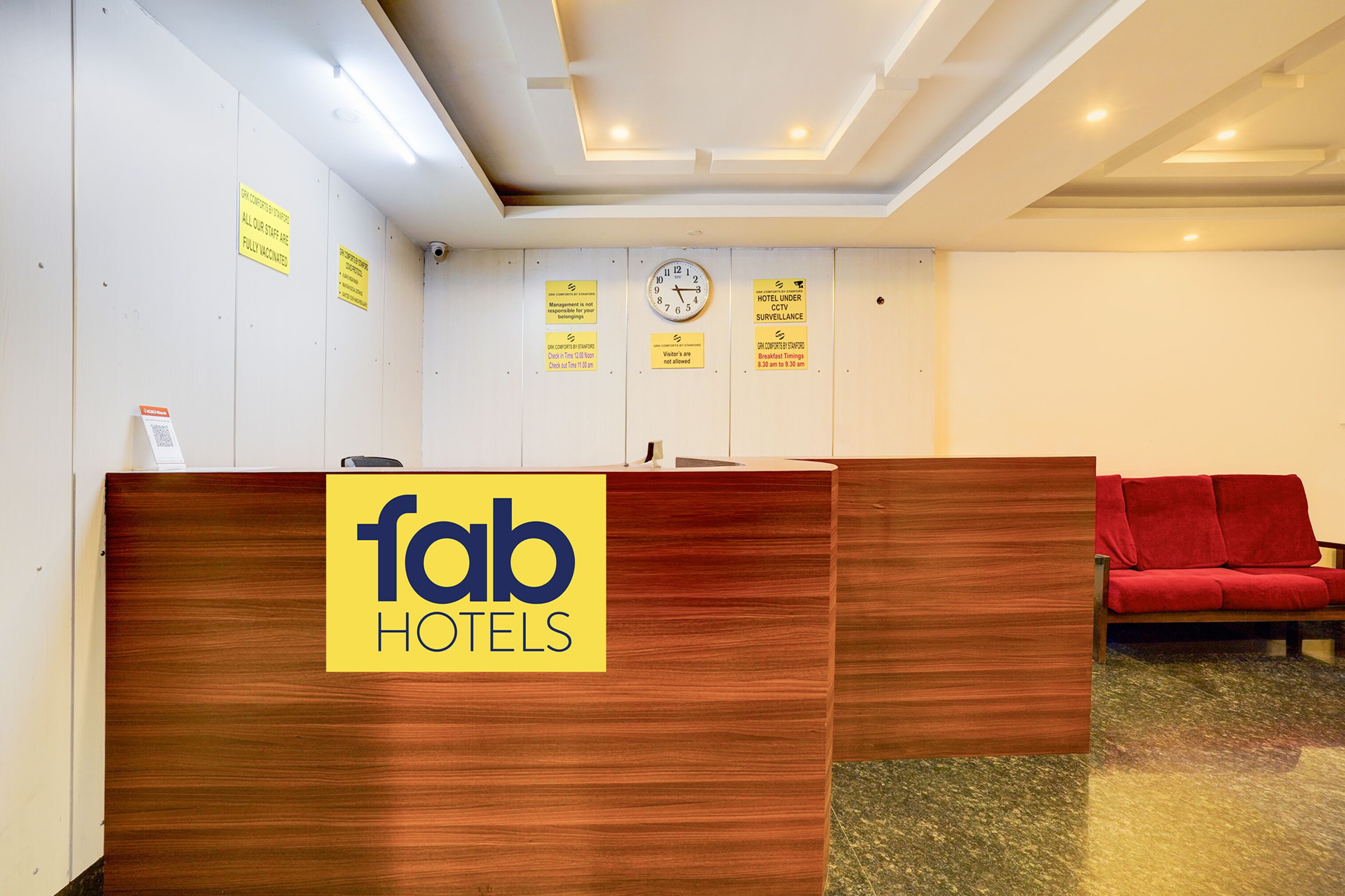 A reception desk with a 'fab hotels' sign, a clock, and several informational signs on the wall.