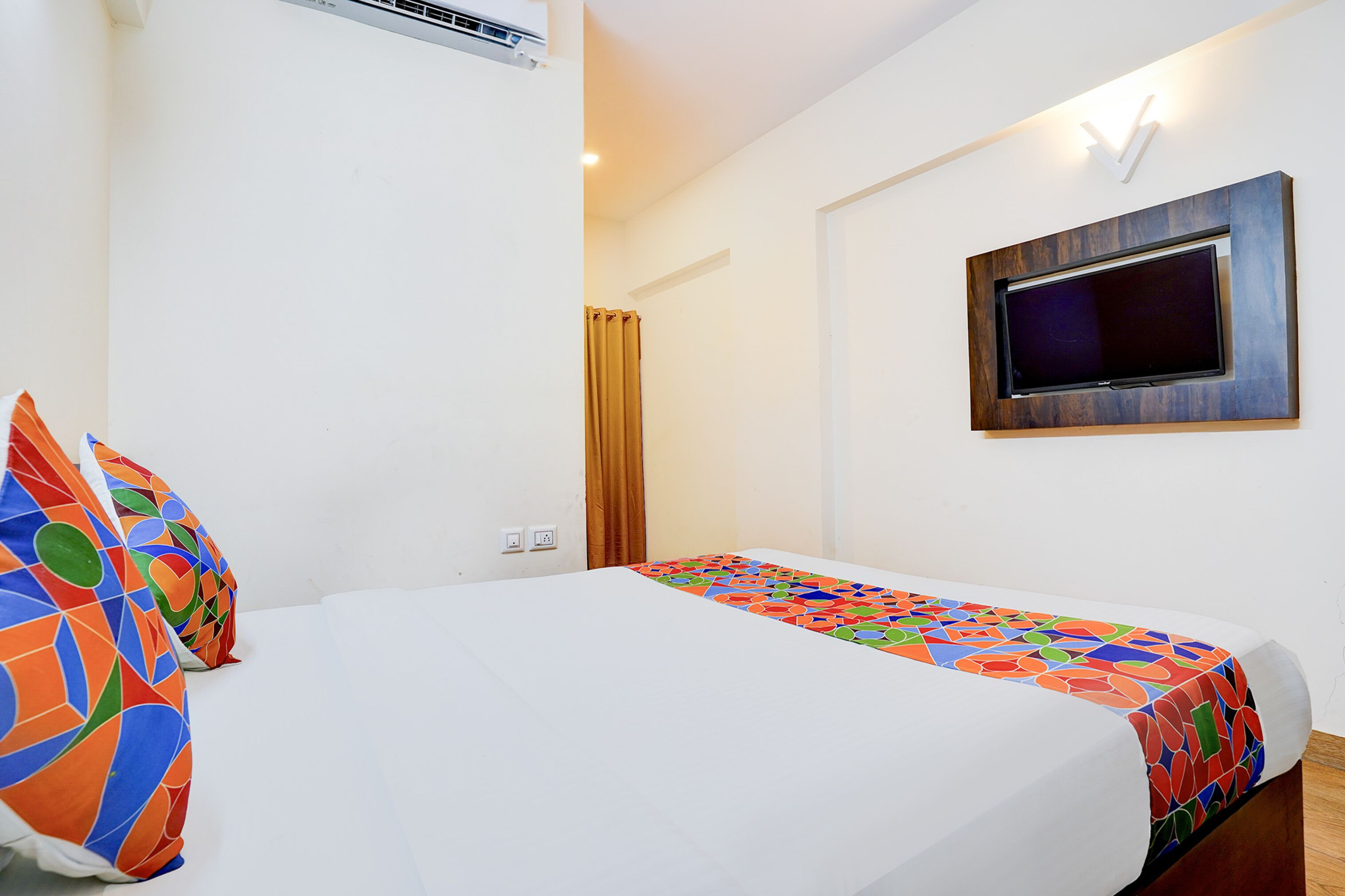 Una camera d'albergo con un letto, una TV a muro e una finestra con tende.