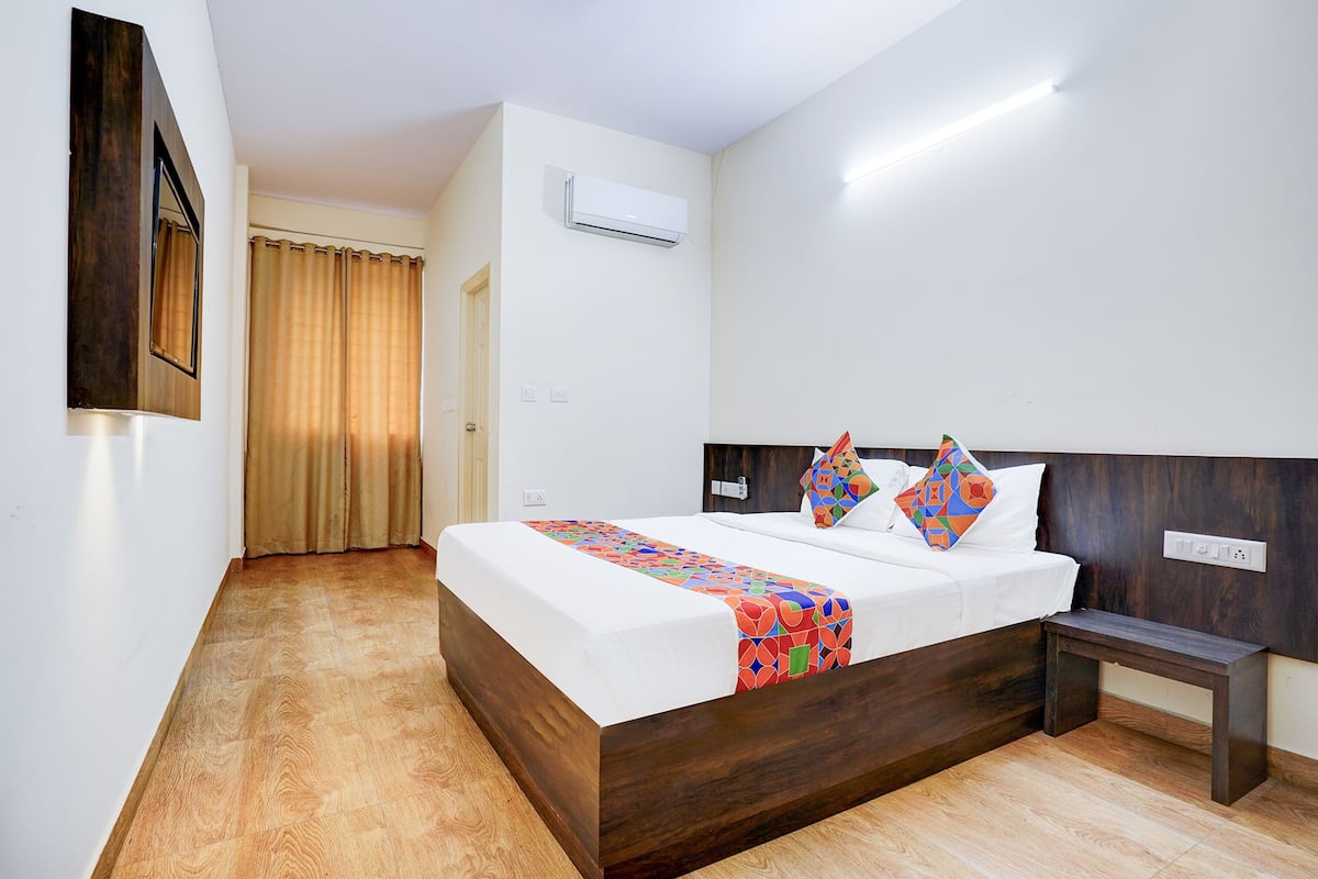 A modern hotel room with a wooden bed, a bedside table, and a large window with curtains.