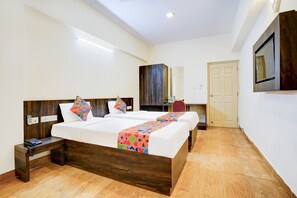 A hotel room with two beds, wooden headboards, a desk, a chair, a mirror, and a door. - Fabhotel Grk Comforts (Bengaluru)