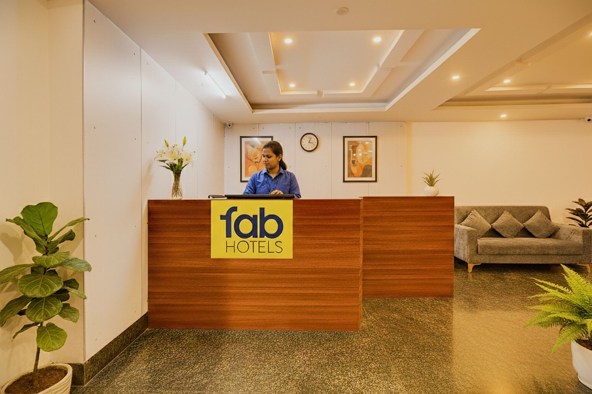 Eine Rezeption mit einem Schild mit der Aufschrift 'fab hotels' in einer Hotelhalle mit einer Couch und Blumentöpfen.