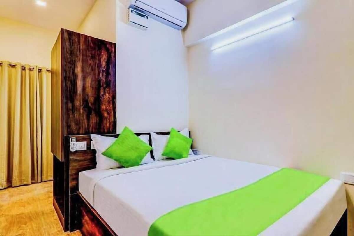 A hotel room with a bed, a wardrobe, an air conditioning unit, and a window with curtains.