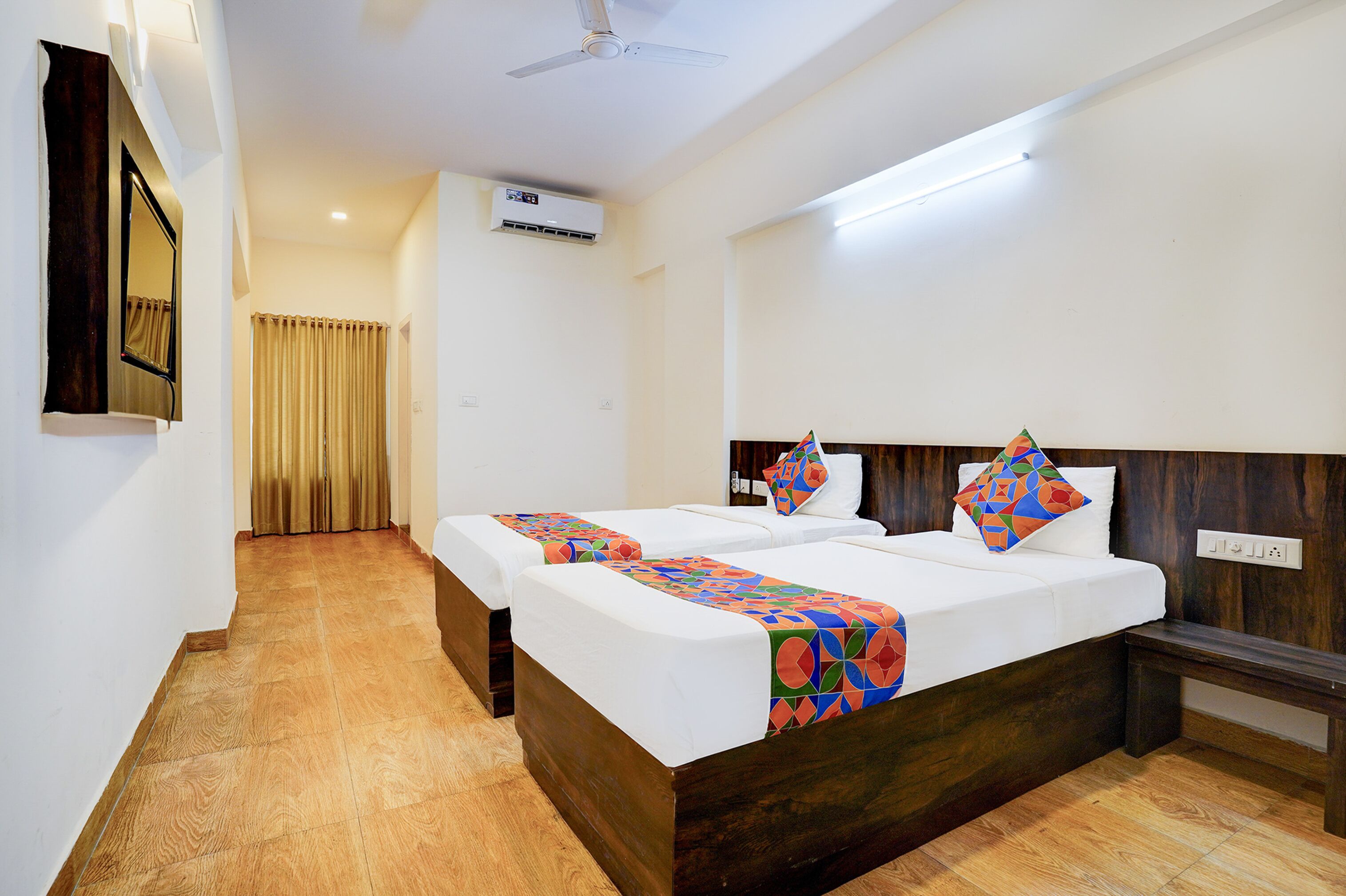 A hotel room with two beds, a ceiling fan, an air conditioning unit, and a wooden bench.