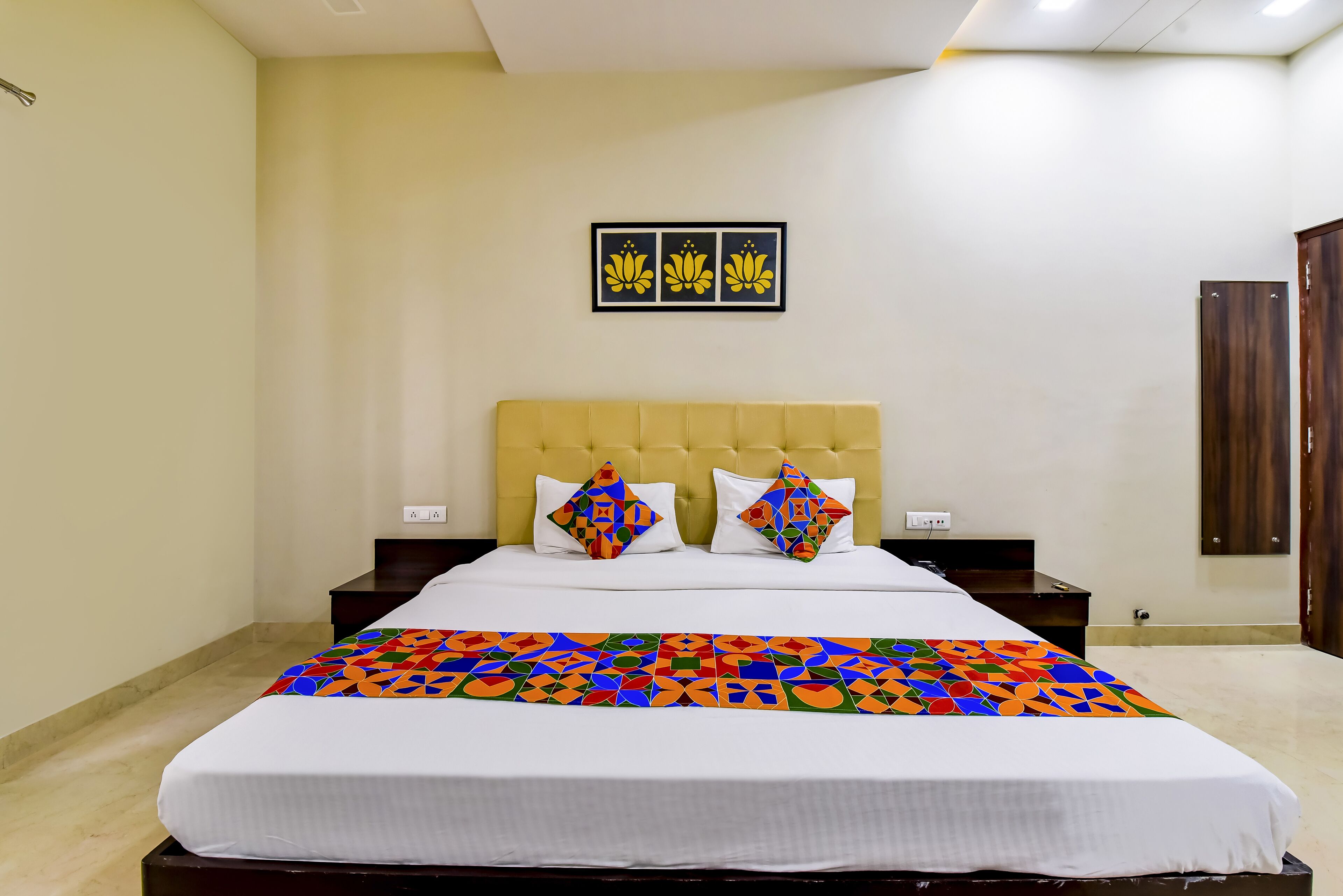 A neatly made bed with a colorful geometric-patterned bedspread, a yellow headboard, and two decorative pillows.
