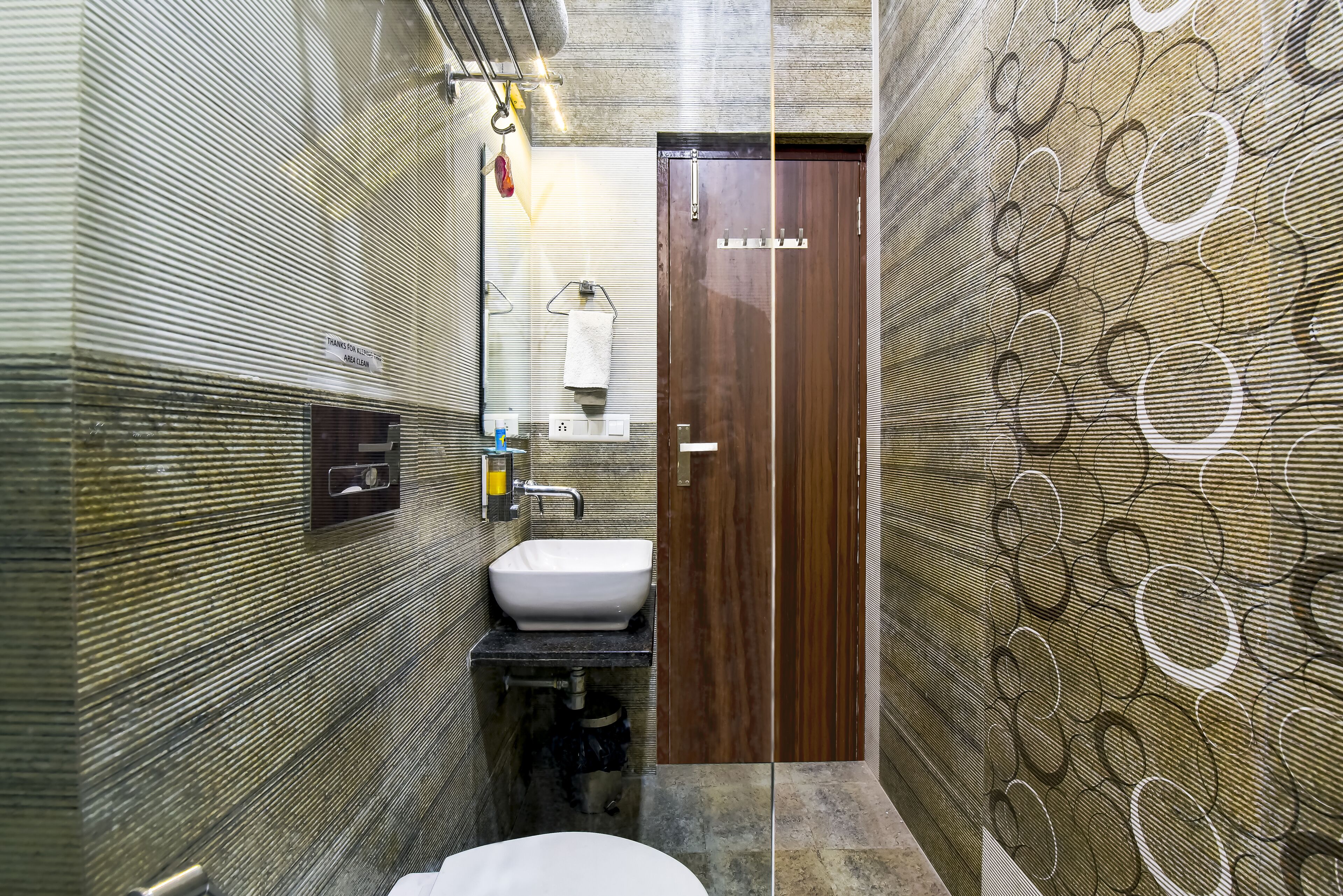 A modern bathroom with a wooden door, a white sink, and a towel rack.