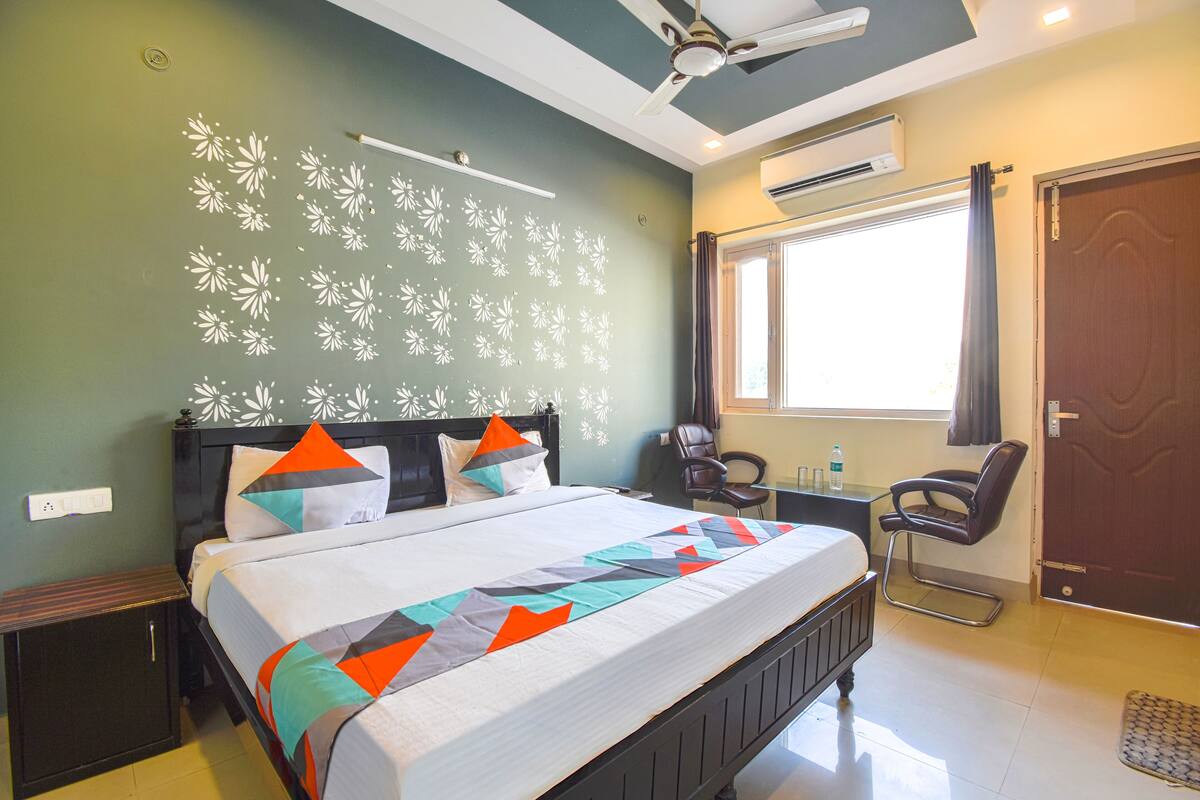 Quarto de hotel com cama, escrivaninha, cadeira, janela e porta.