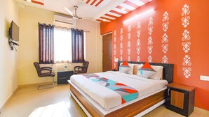 A hotel room with a large bed, a desk with a chair, a TV, and a window with curtains.