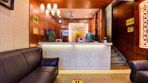 A hotel reception area with a reception desk, two sofas, a clock, and a staircase. - Oriva Suvee Boutique (Bengaluru)