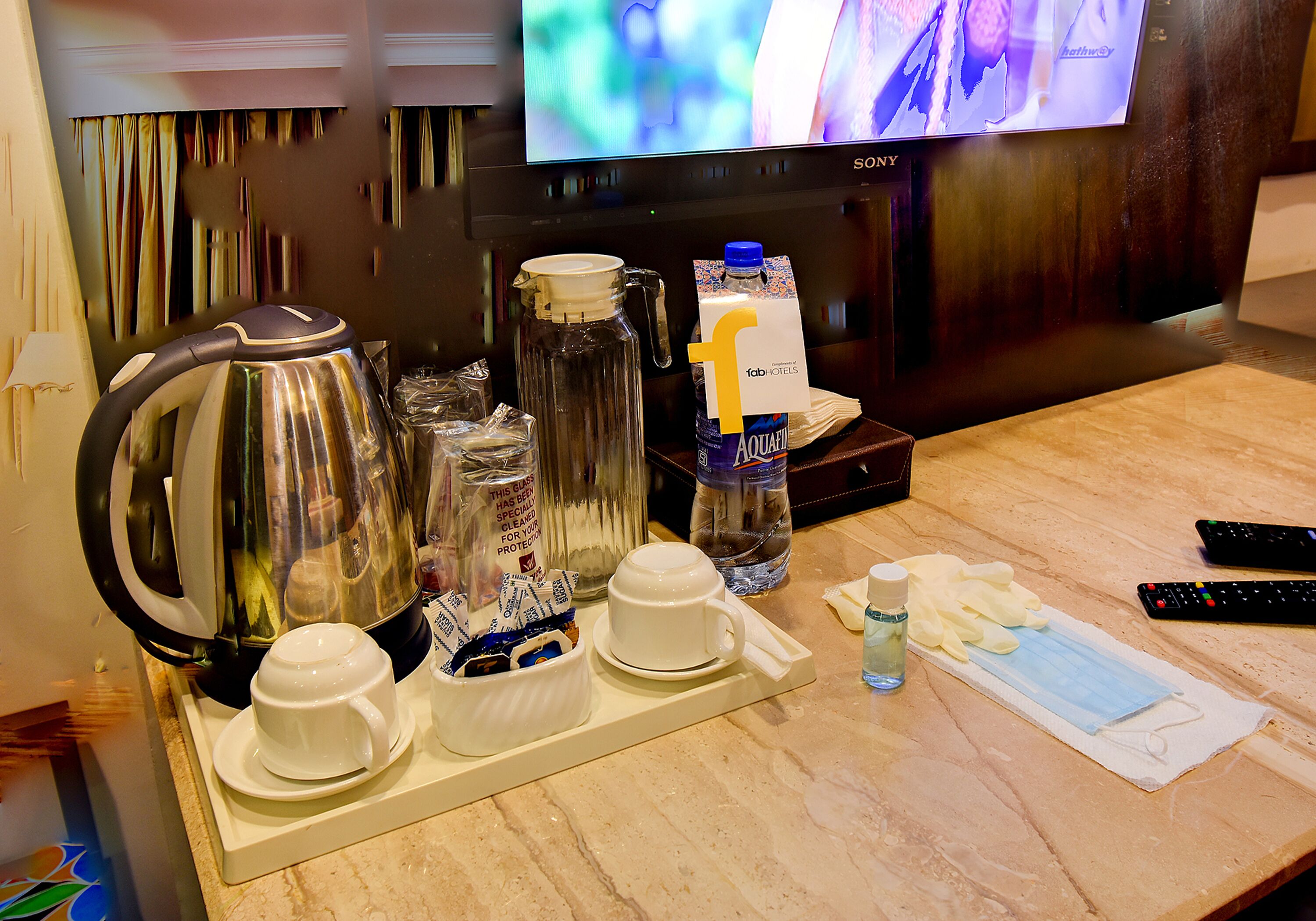 A hotel room with a coffee station, a television, and a water bottle.