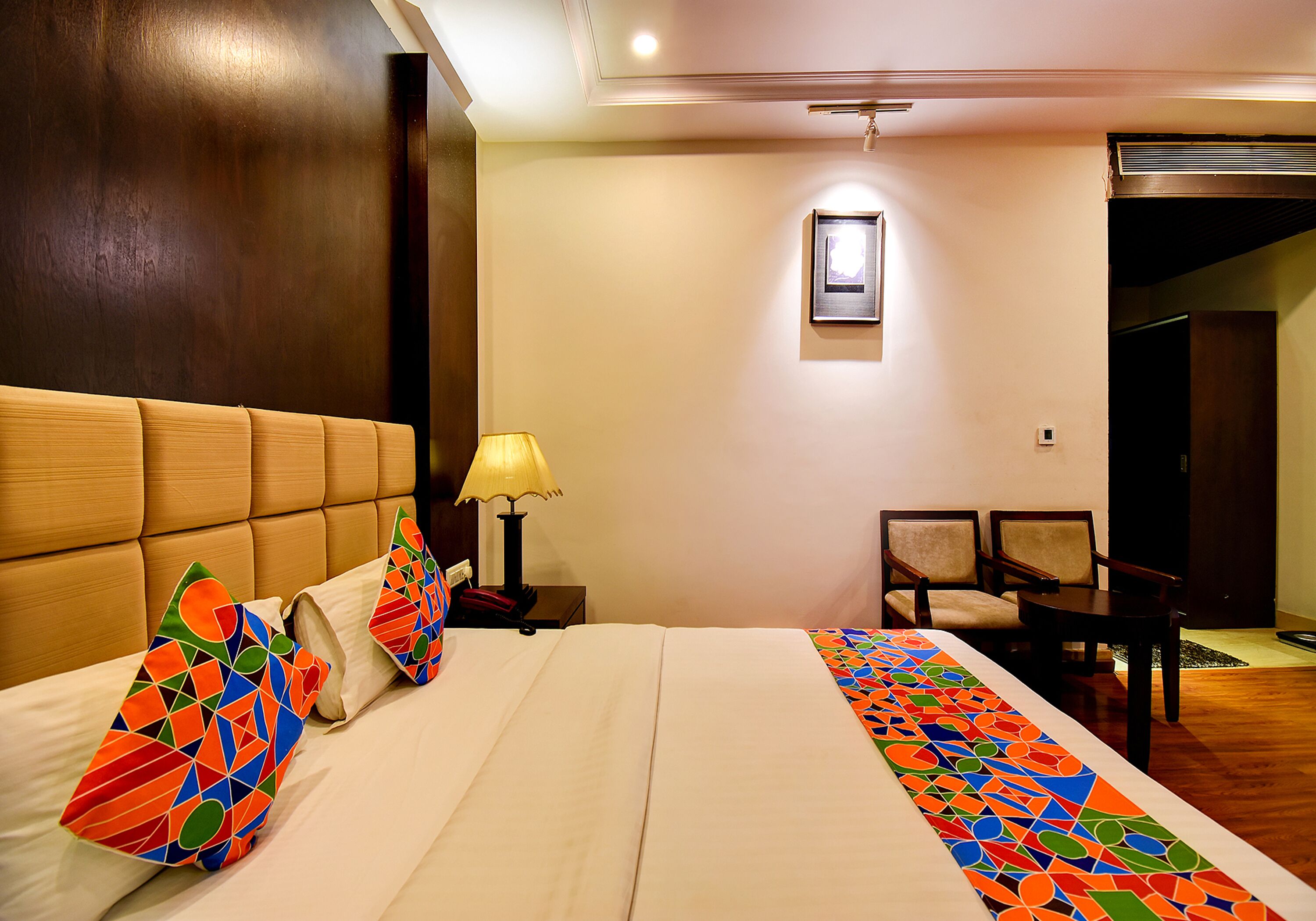 A hotel room with a large bed, a nightstand with a lamp, a chair, and a small table.